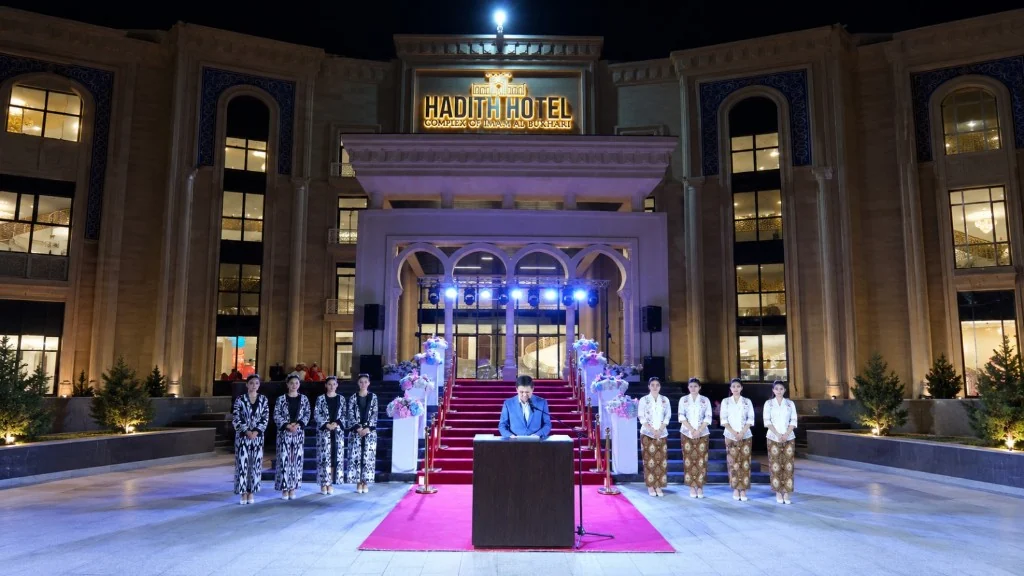 The HADITH Hotel soft-opening ceremony: a speaker at the podium, flanked by performers in Uzbek dress and Indonesian kebaya batik.