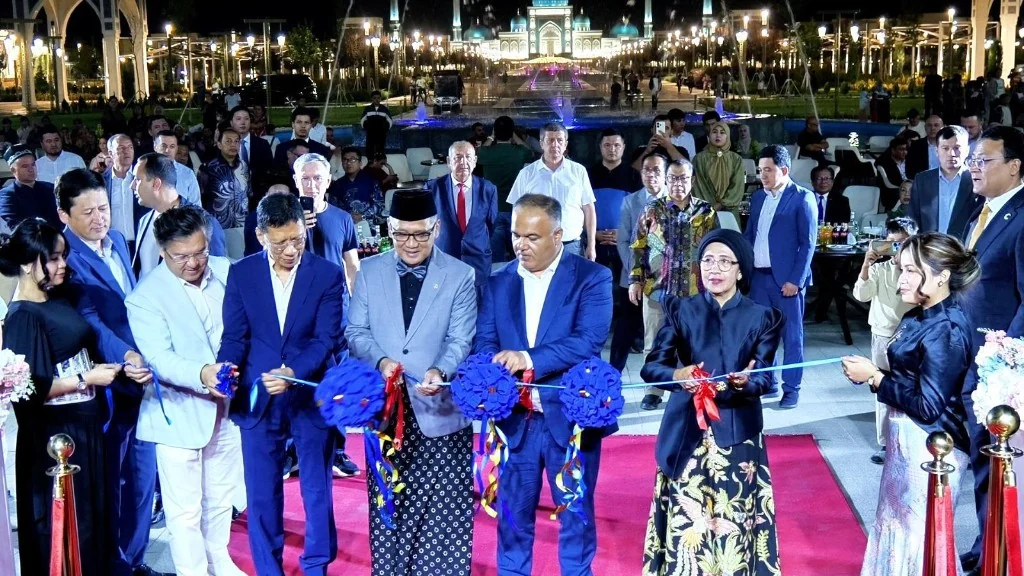 Officials cut a ceremonial ribbon at the HADITH Hotel soft opening in Samarkand, with the Imam Al-Bukhari Complex illuminated behind them.
